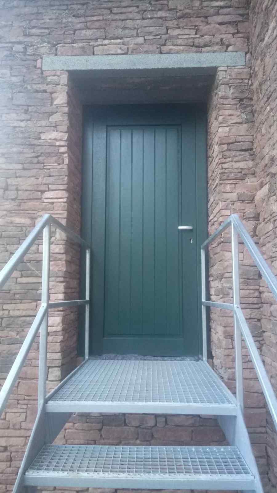 Eine grüne Tür an einem Backsteingebäude, zu der eine Treppe hinaufführt.