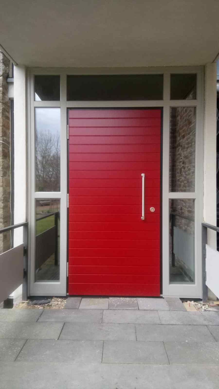 Vor einem Gebäude steht eine rote Tür mit einer weißen Klinke.