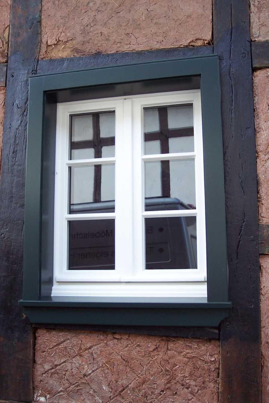 An einer Ziegelwand befindet sich ein weißes Fenster mit schwarzem Rahmen.