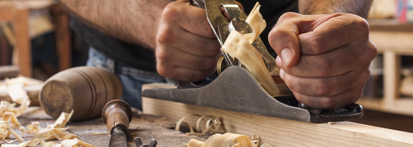 Ein Mann hobelt mit einem Hobel ein Stück Holz.