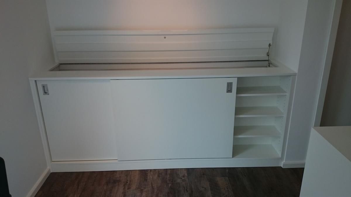 Ein weißer Schrank mit Schiebetüren und Regalen in einem Zimmer.