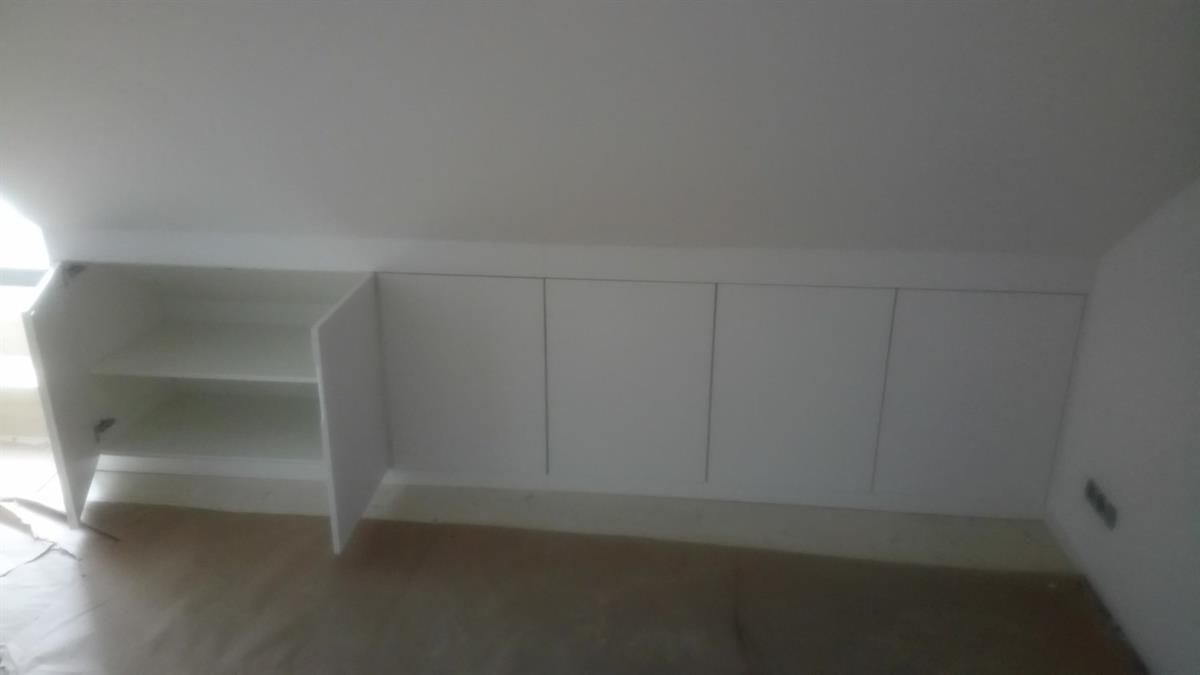 Ein Raum mit weißen Schränken und Regalen unter einer Dachschräge.