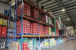 Interior de almacén lleno de estantes repletos de cajas, cajones y palés con productos envasados.