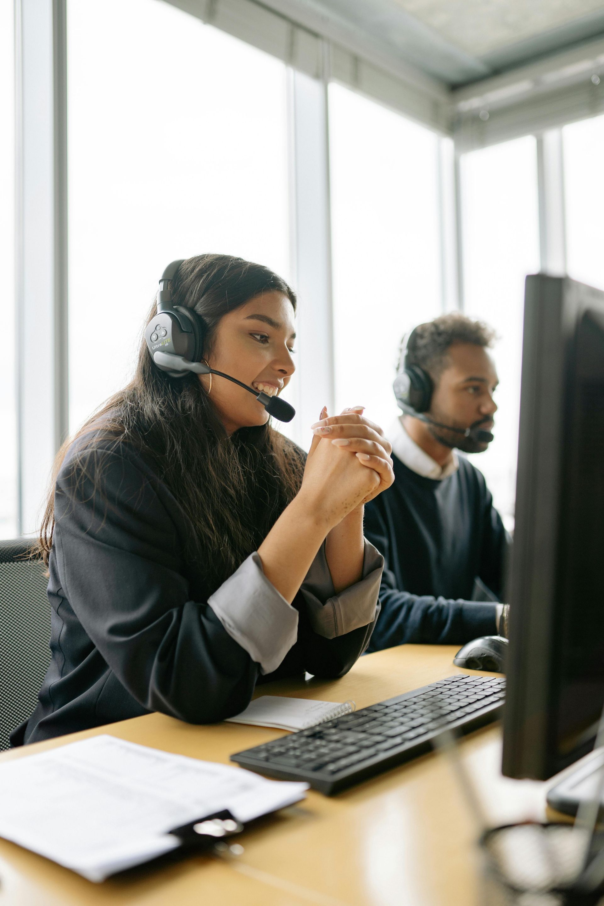 Mujer con auriculares, hablando por micrófono, sentada en un escritorio con una computadora.