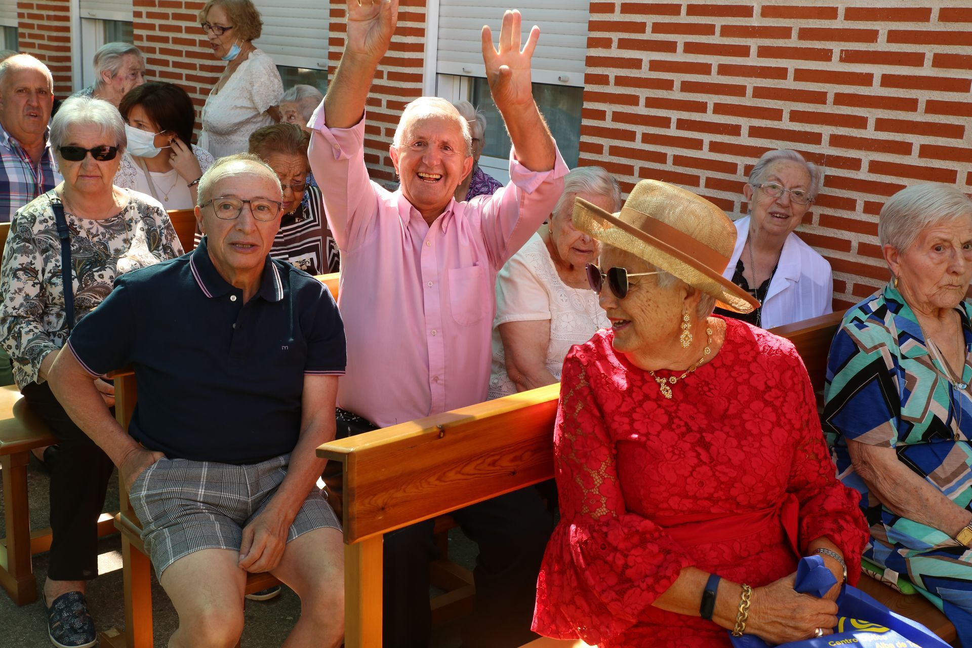 Un grupo de personas mayores están sentadas en un banco con un hombre agitando la mano.