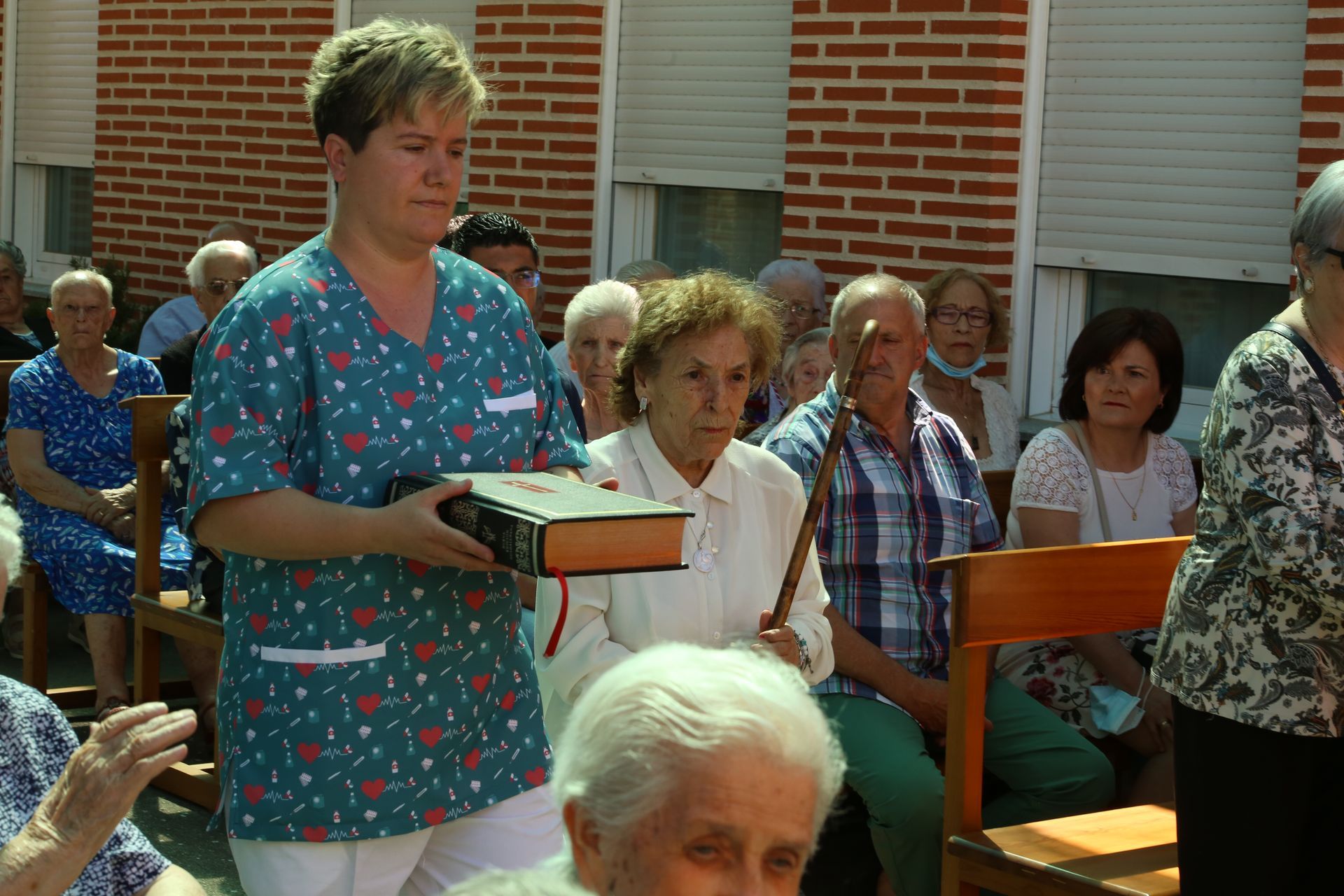 Una mujer con una bata quirúrgica sostiene un libro frente a un grupo de personas.
