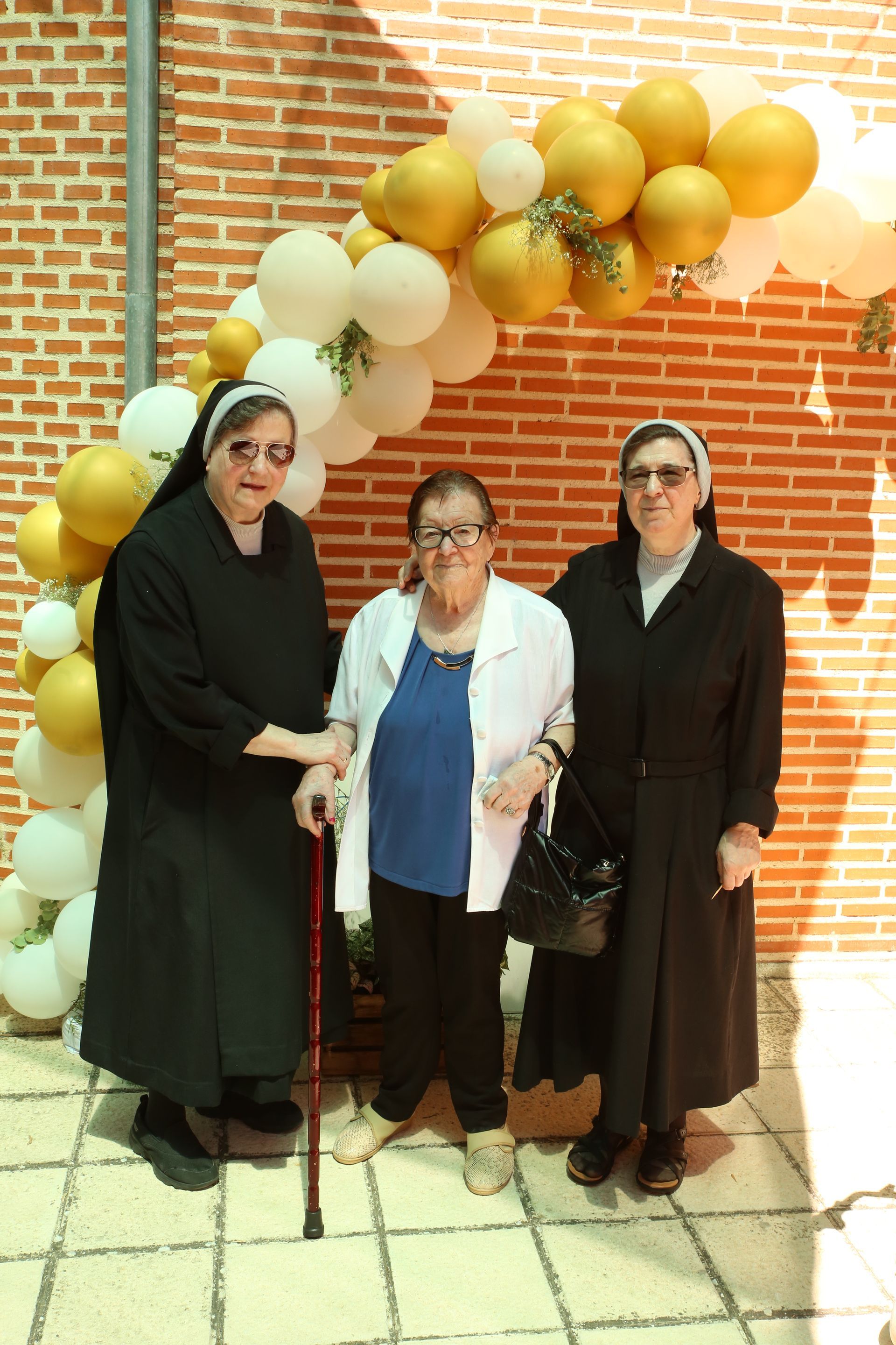 Tres mujeres paradas frente a una pared de ladrillos con globos.