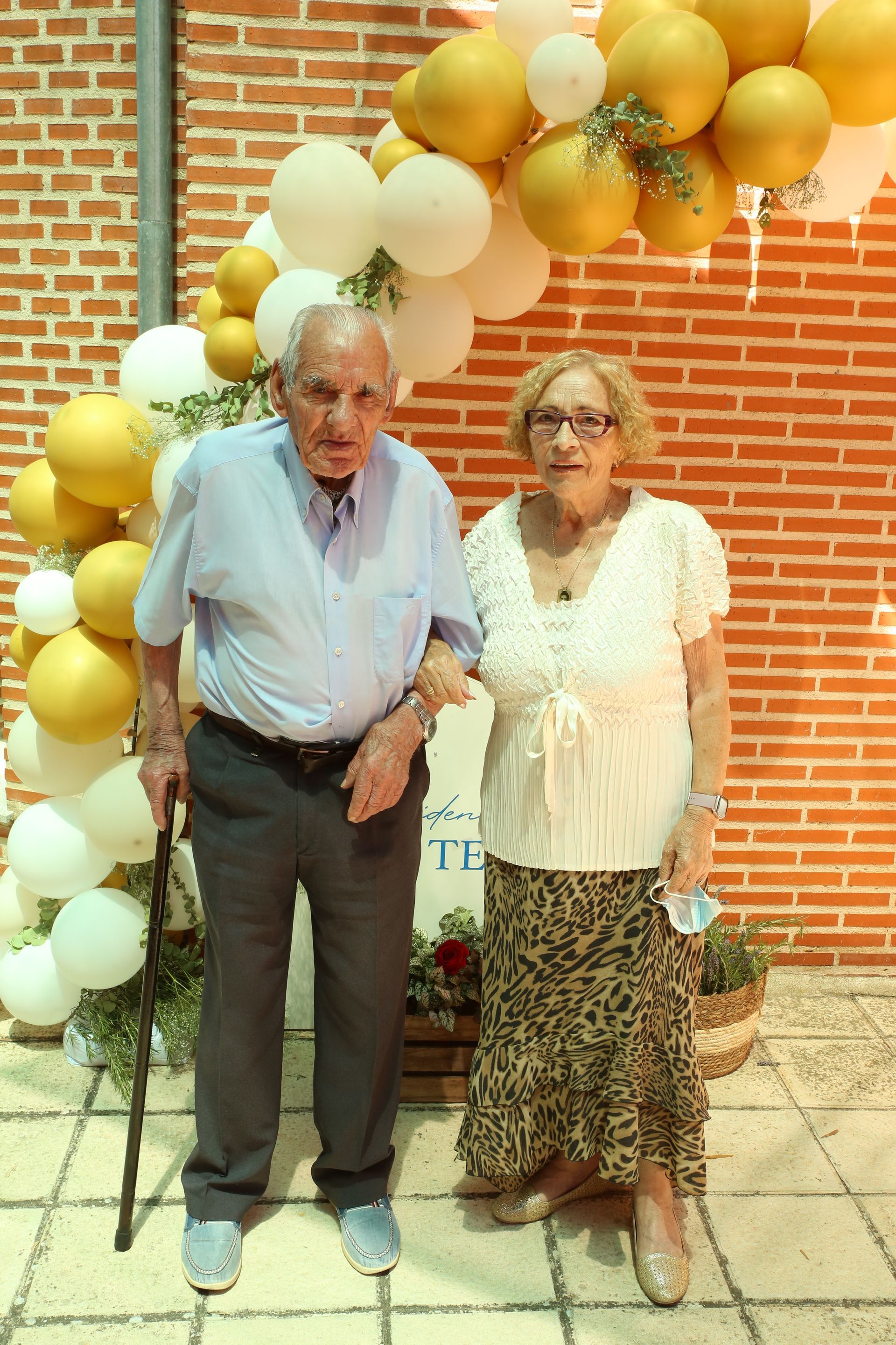 Un hombre y una mujer de pie frente a una pared de ladrillos con globos.