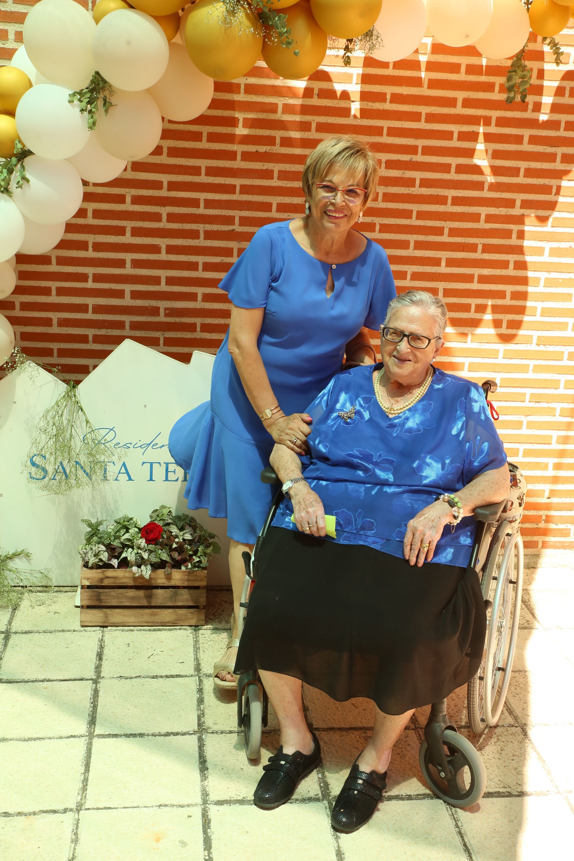 Una mujer parada junto a una mujer mayor en silla de ruedas.