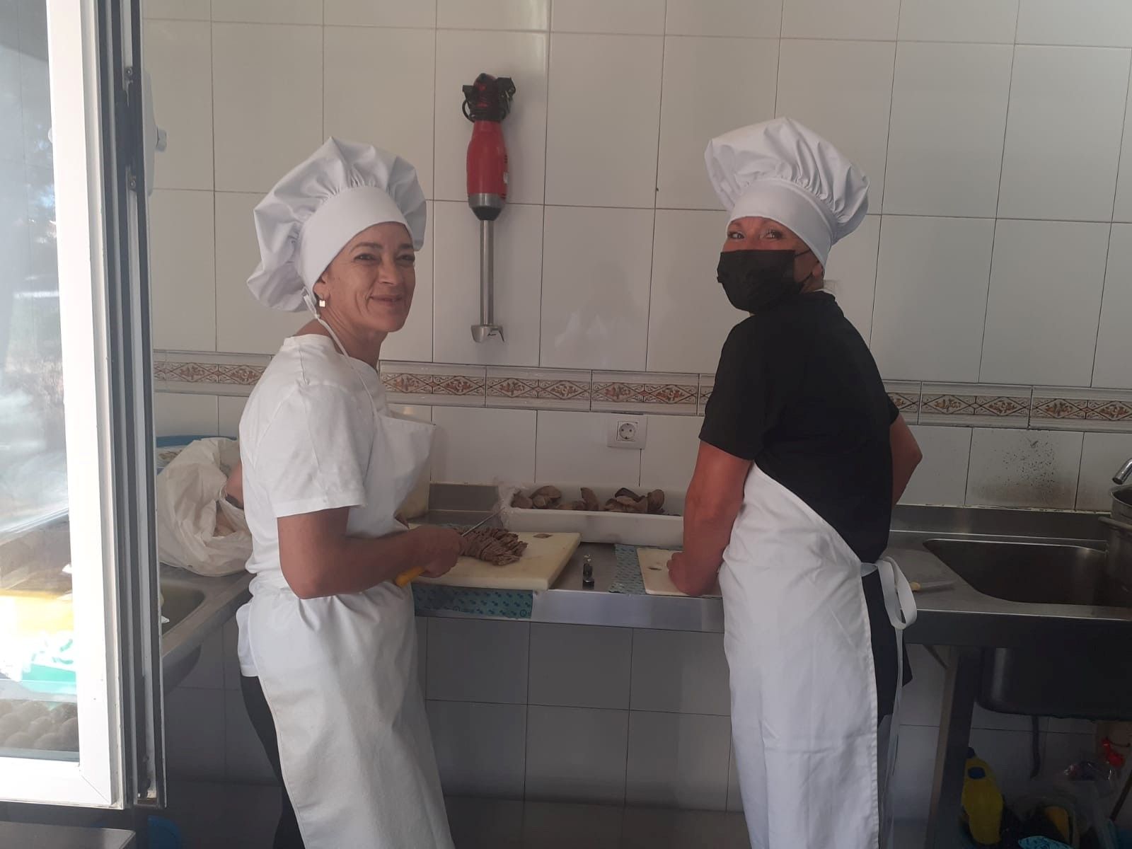 Dos mujeres con gorros y delantales de chef están paradas en una cocina.