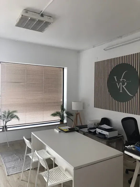 Una habitación con un escritorio, sillas y una ventana grande.