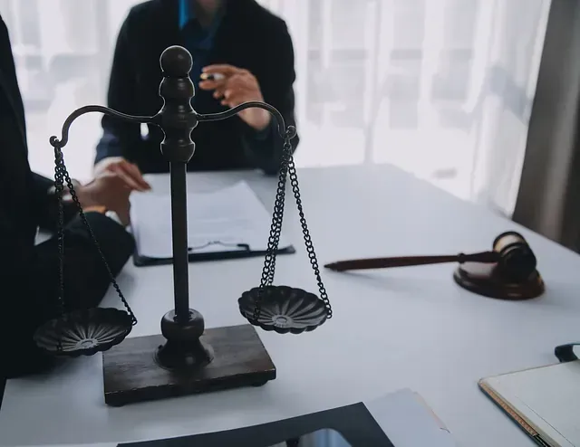 Una mujer está sentada a una mesa con una balanza de justicia y un mazo.