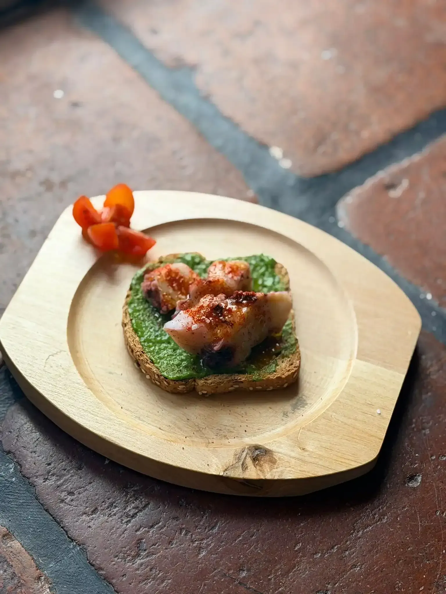 Pequeño aperitivo servido en un plato redondo de madera con una tostada 