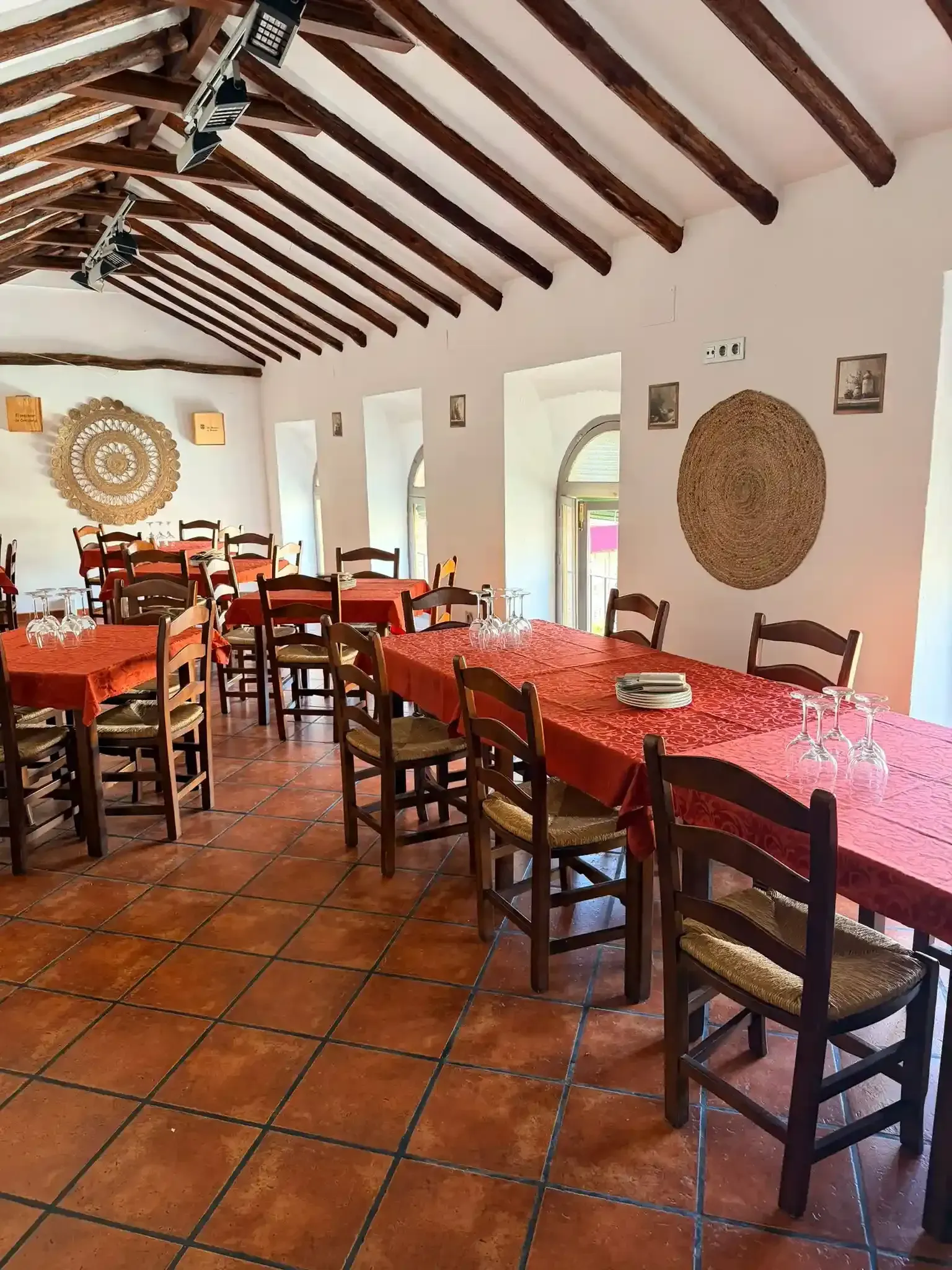 Comedor rústico con mesas de madera, suelo de terracota y techo con vigas vistas.