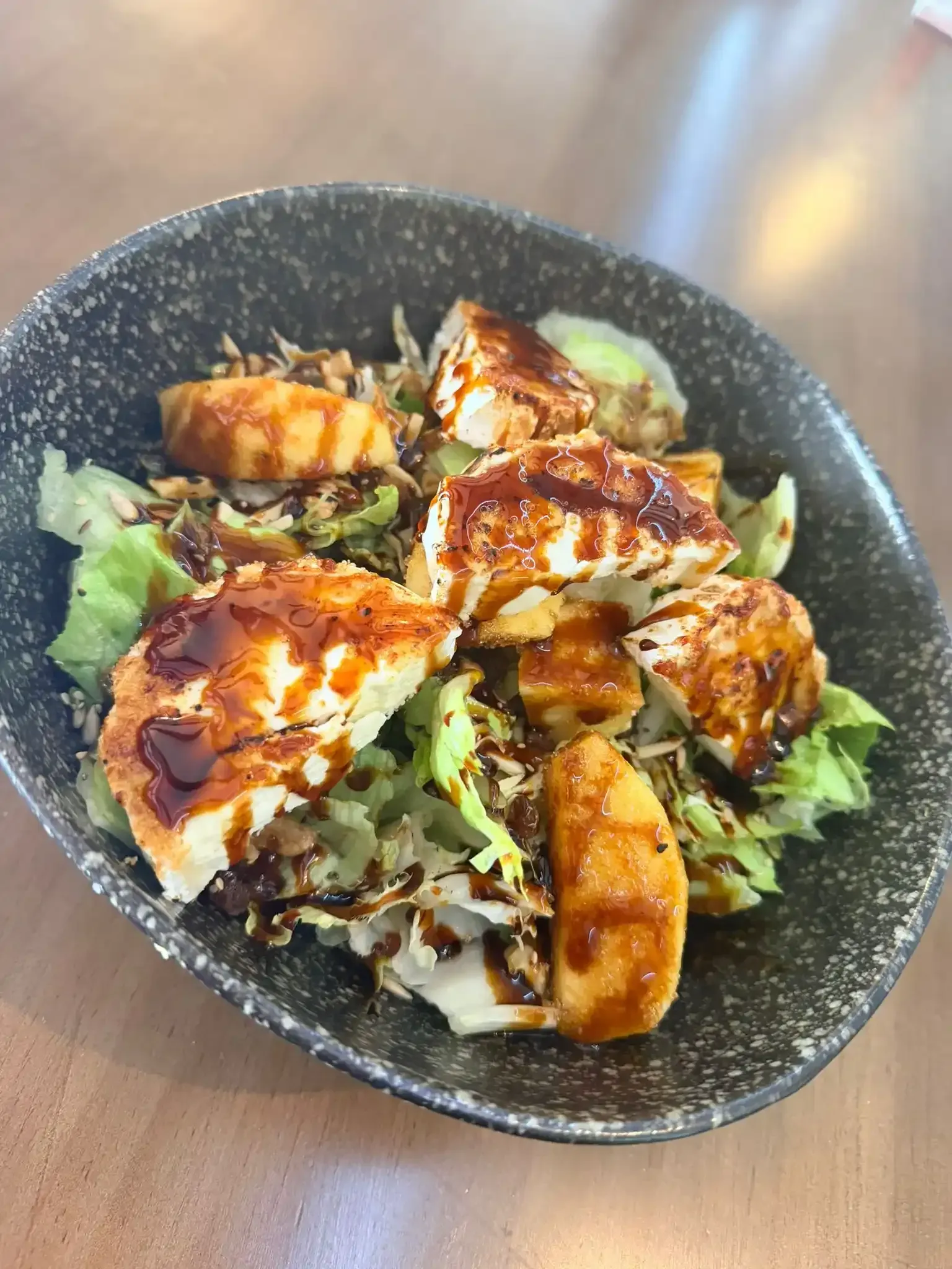 Pollo a la parrilla sobre lechuga rallada en un tazón negro con salsa rociada.