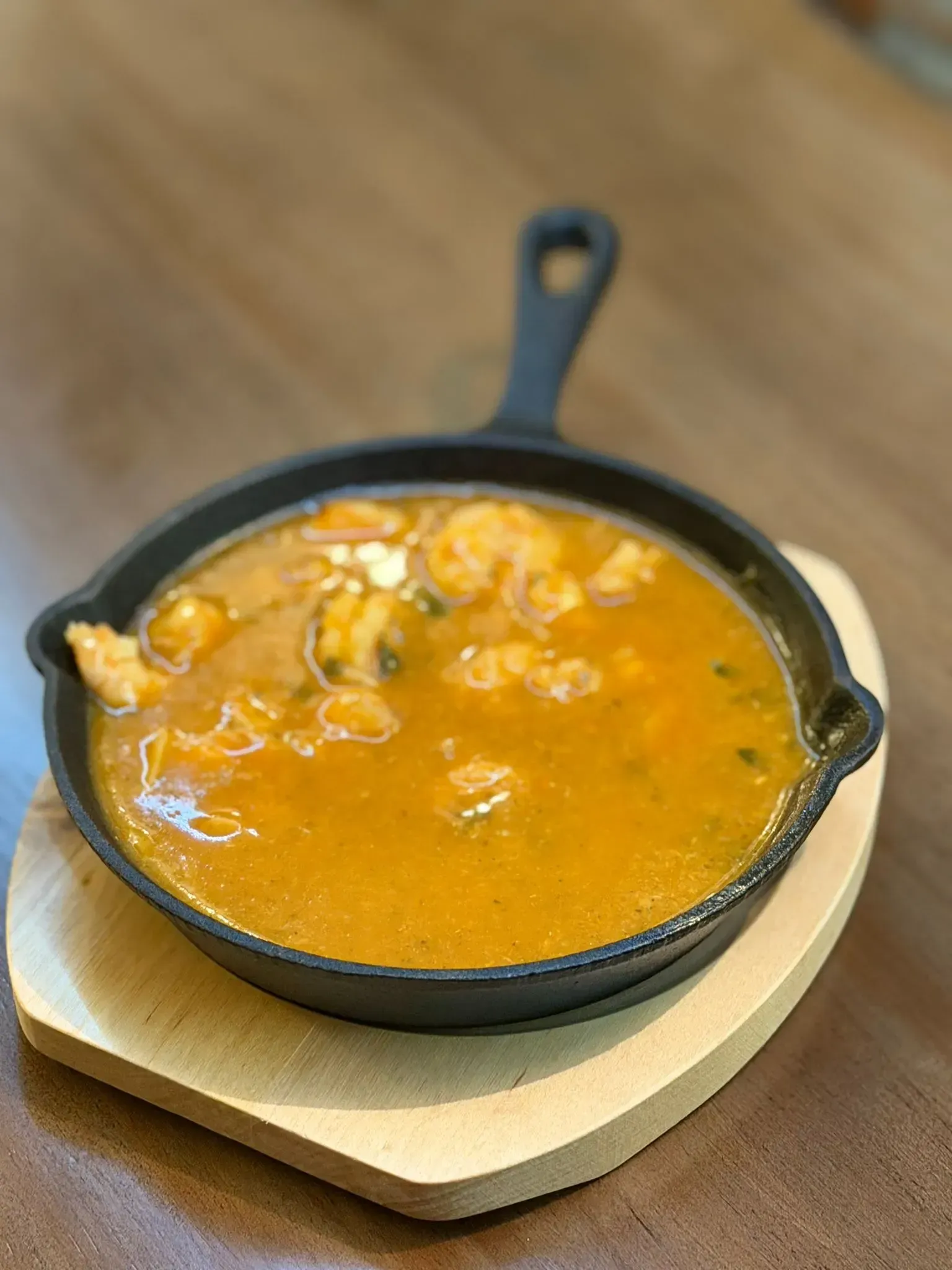 Sartén pequeña de hierro fundido con estofado de naranja sobre un salvamanteles de madera.