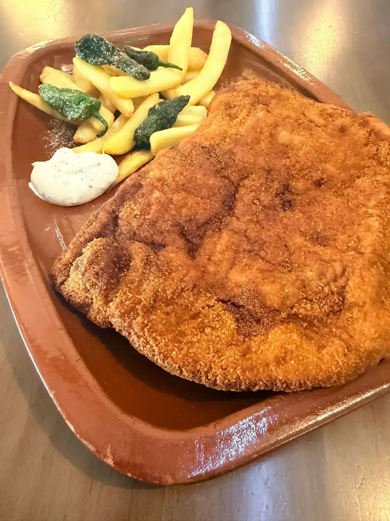 Chuleta empanizada frita con papas fritas y verduras en un plato marrón.