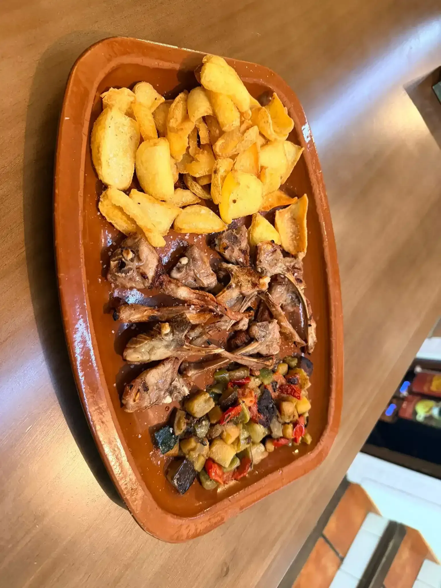 Bandeja con patatas fritas, carne a la parrilla y verduras variadas sobre una mesa de madera.