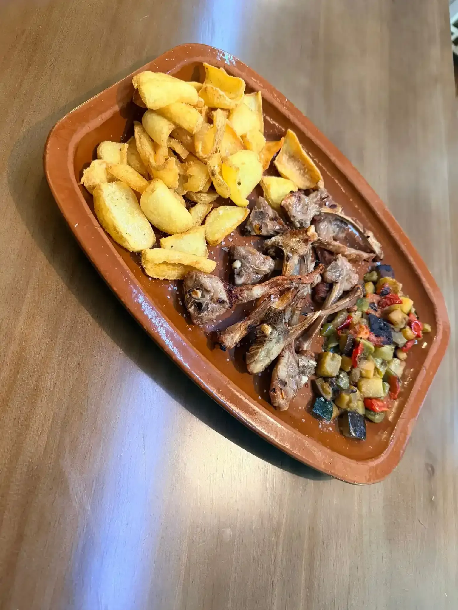Bandeja de carne en rodajas con patatas fritas y verduras variadas sobre una mesa de madera.