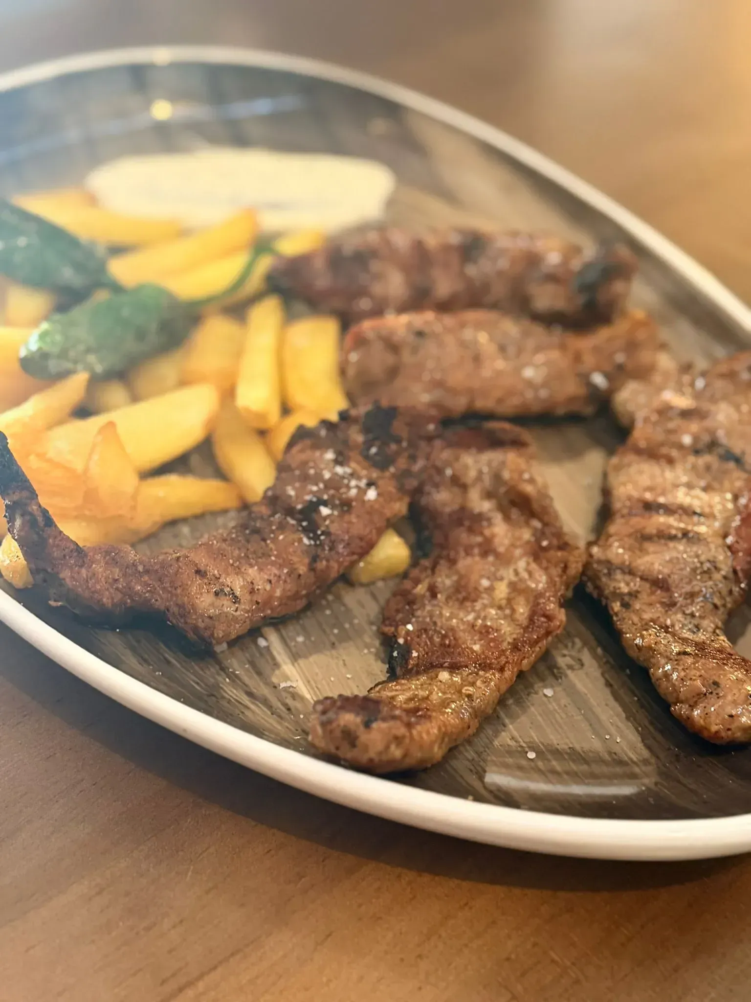 Tiras de carne a la parrilla con patatas fritas y una rodaja de limón en un plato blanco.