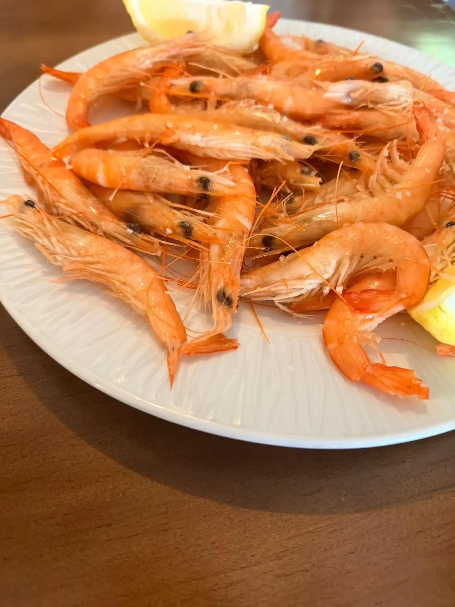 Plato de gambas a la naranja cocidas con rodajas de limón sobre una mesa de madera.