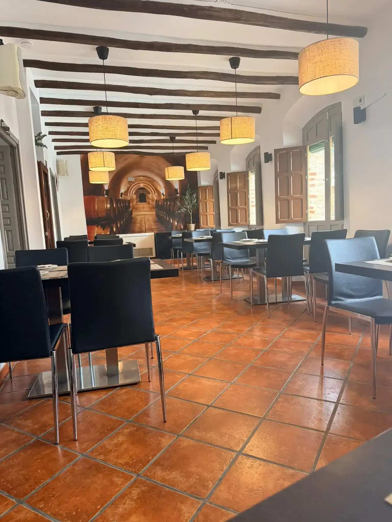 Comedor vacío de un restaurante con suelo de baldosas, sillas negras, sofás azules y lámparas colgantes cálidas.