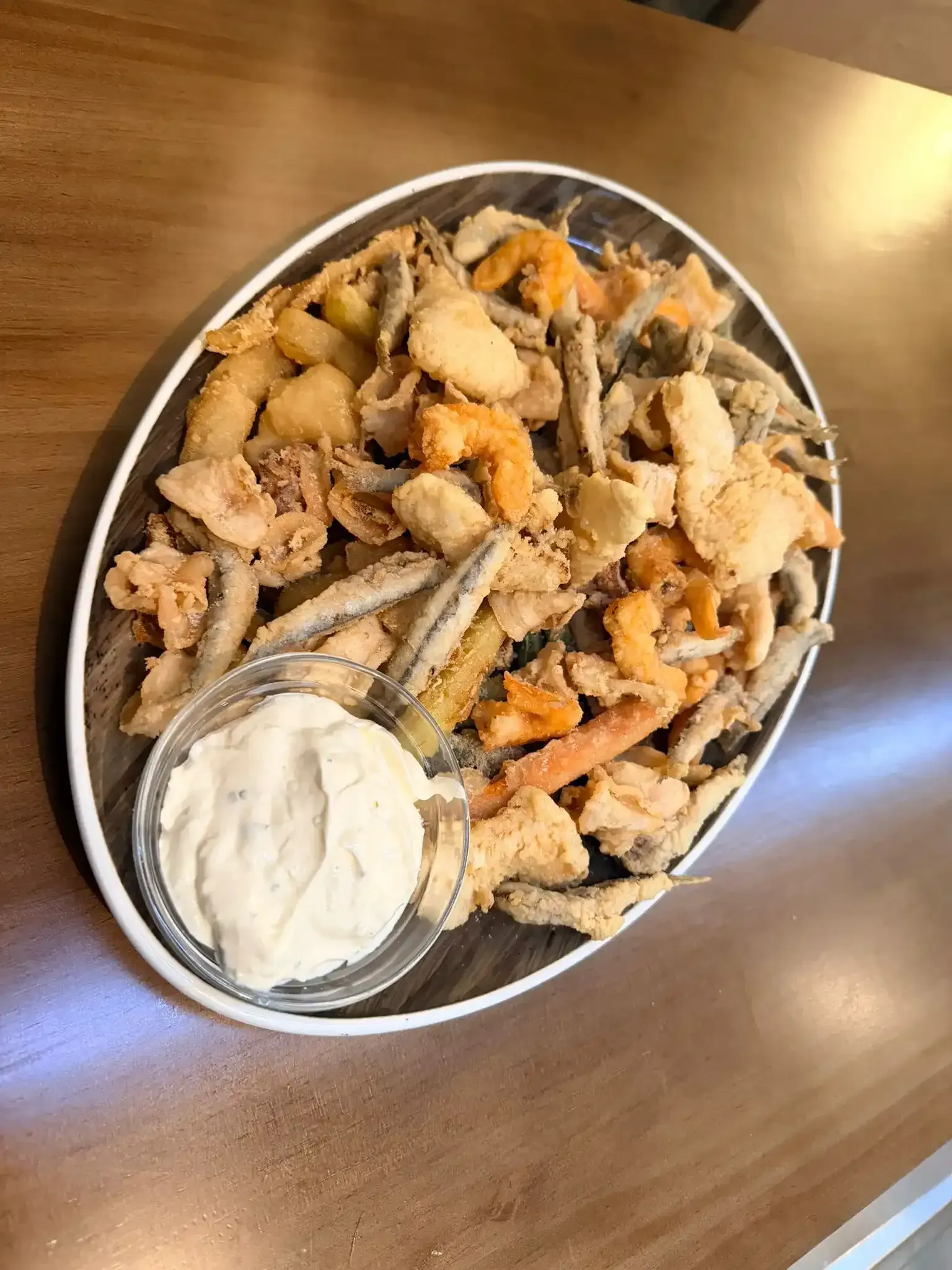 Bandeja de mariscos fritos con una taza de salsa para mojar sobre una mesa de madera.