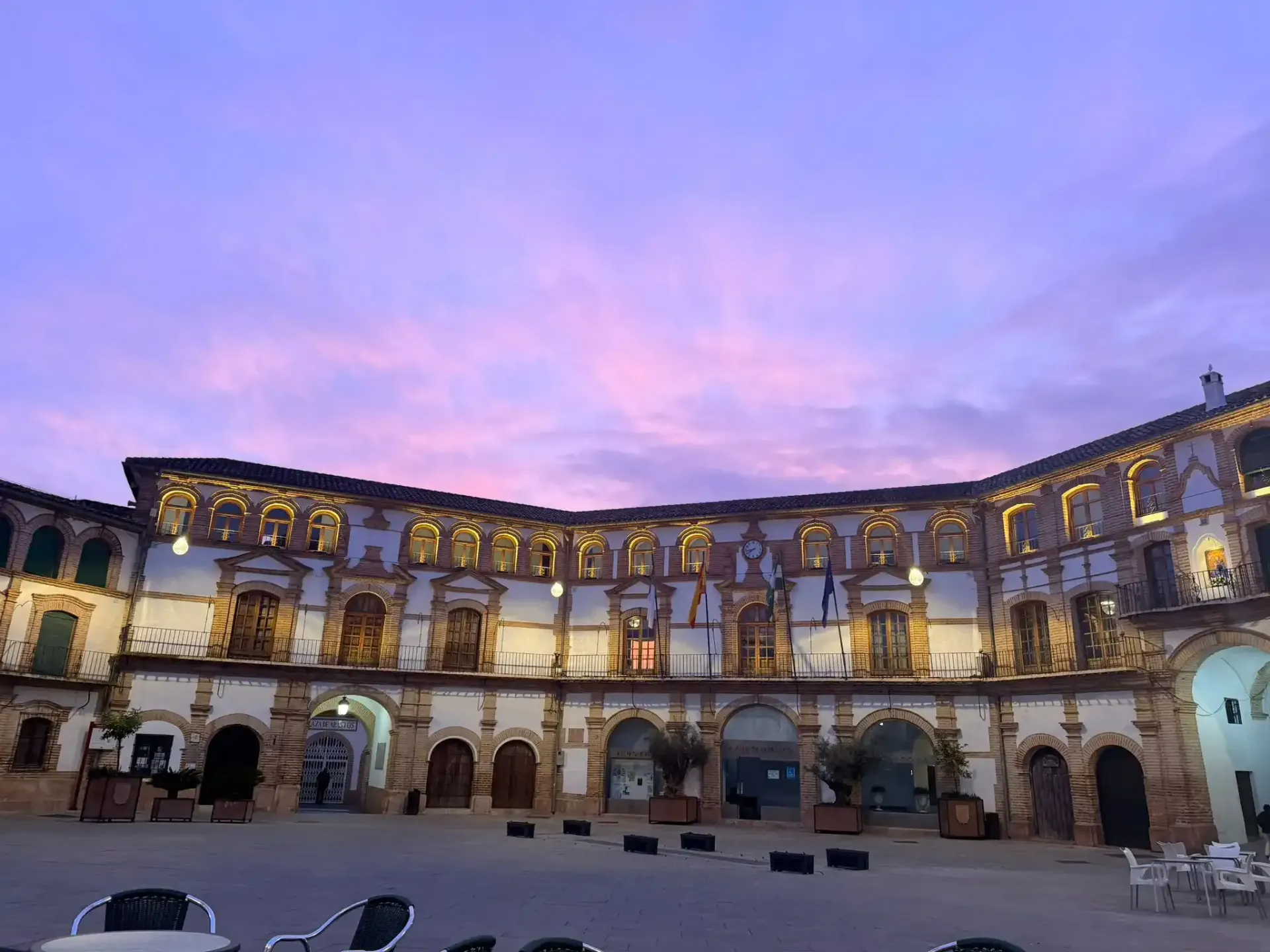 Patio iluminado de un gran edificio arqueado al anochecer bajo un cielo rosa-púrpura.