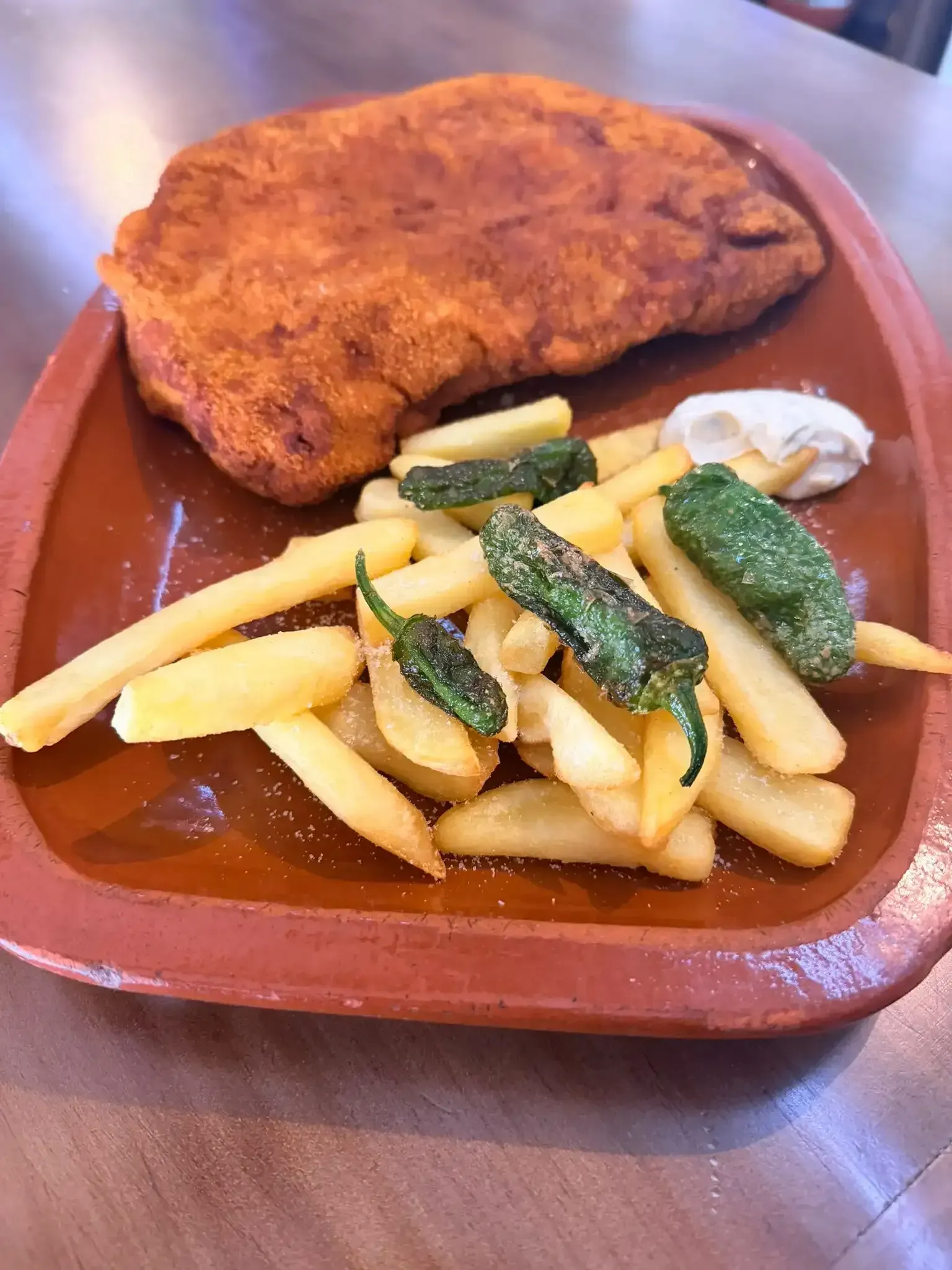 Escalope empanado con patatas fritas y pimientos verdes en un plato marrón.