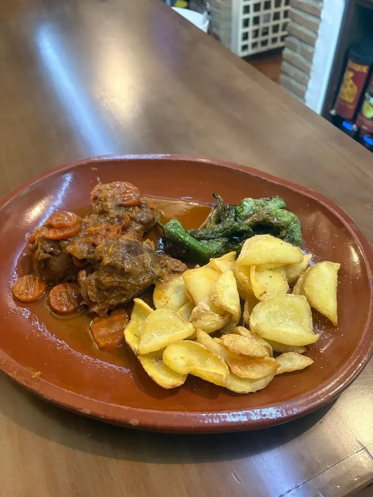 Curry emplatado con carne, patatas y verduras en un plato marrón sobre una mesa de madera.