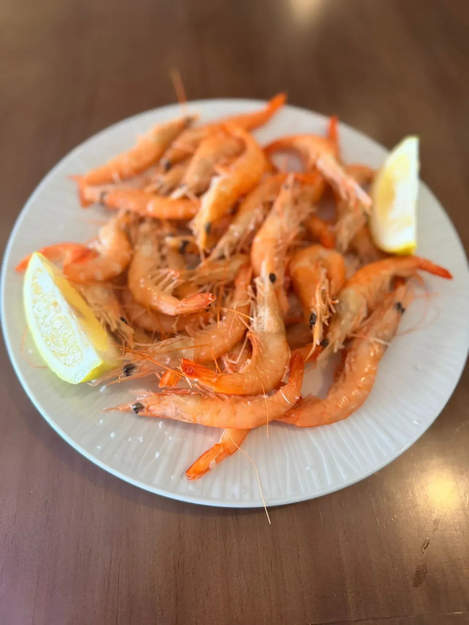 Plato de gambas cocidas con rodajas de limón sobre una mesa de madera.