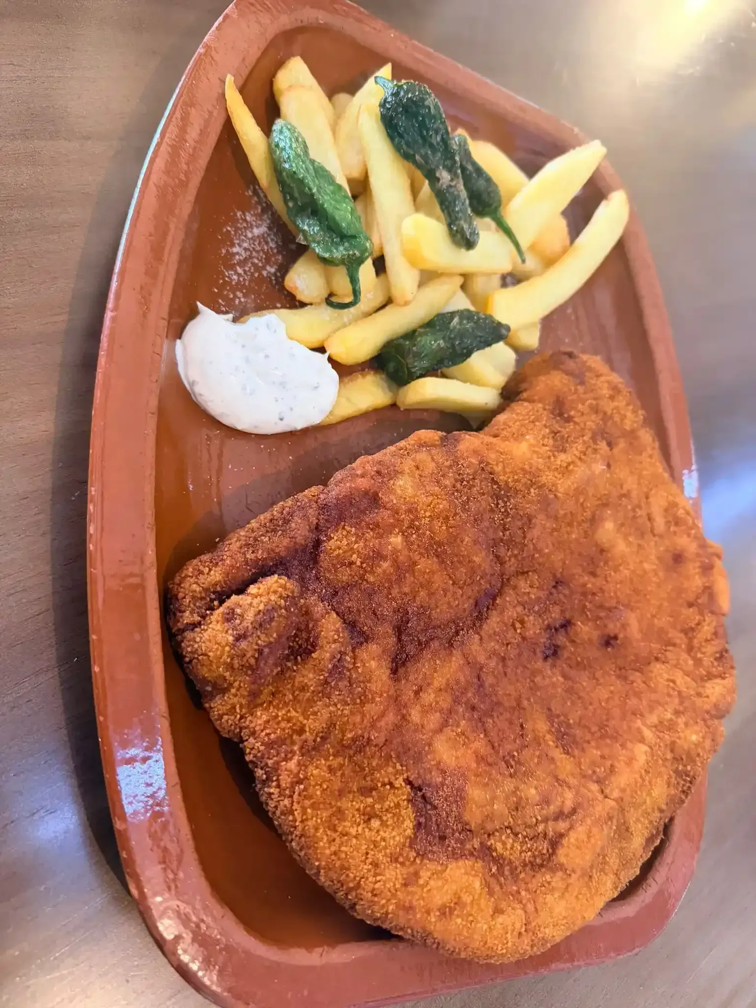 Chuleta empanada con papas fritas y una cucharada de salsa blanca en una bandeja marrón.