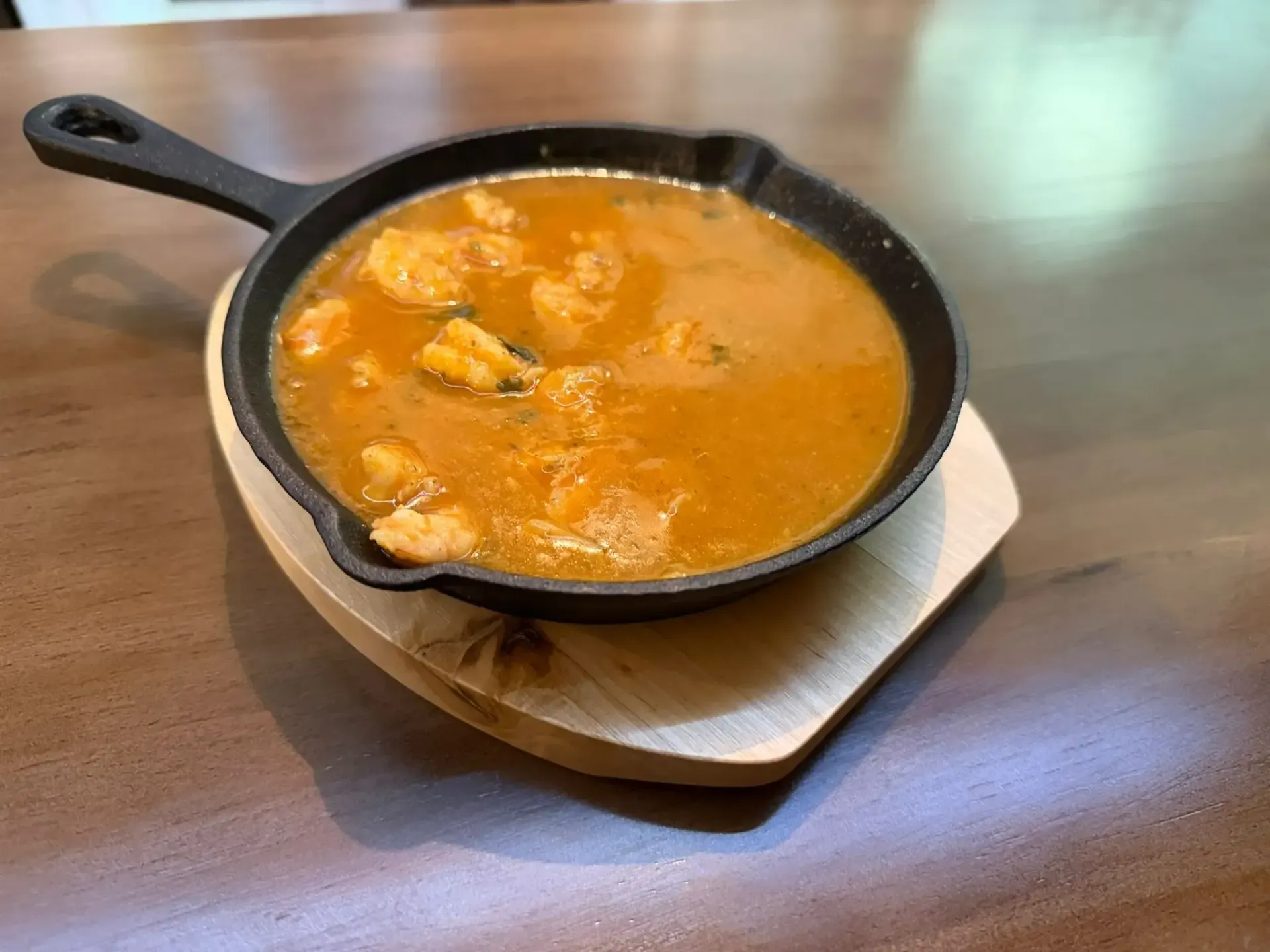 Sartén negra con sopa de naranja sobre un posavasos de madera en una mesa.