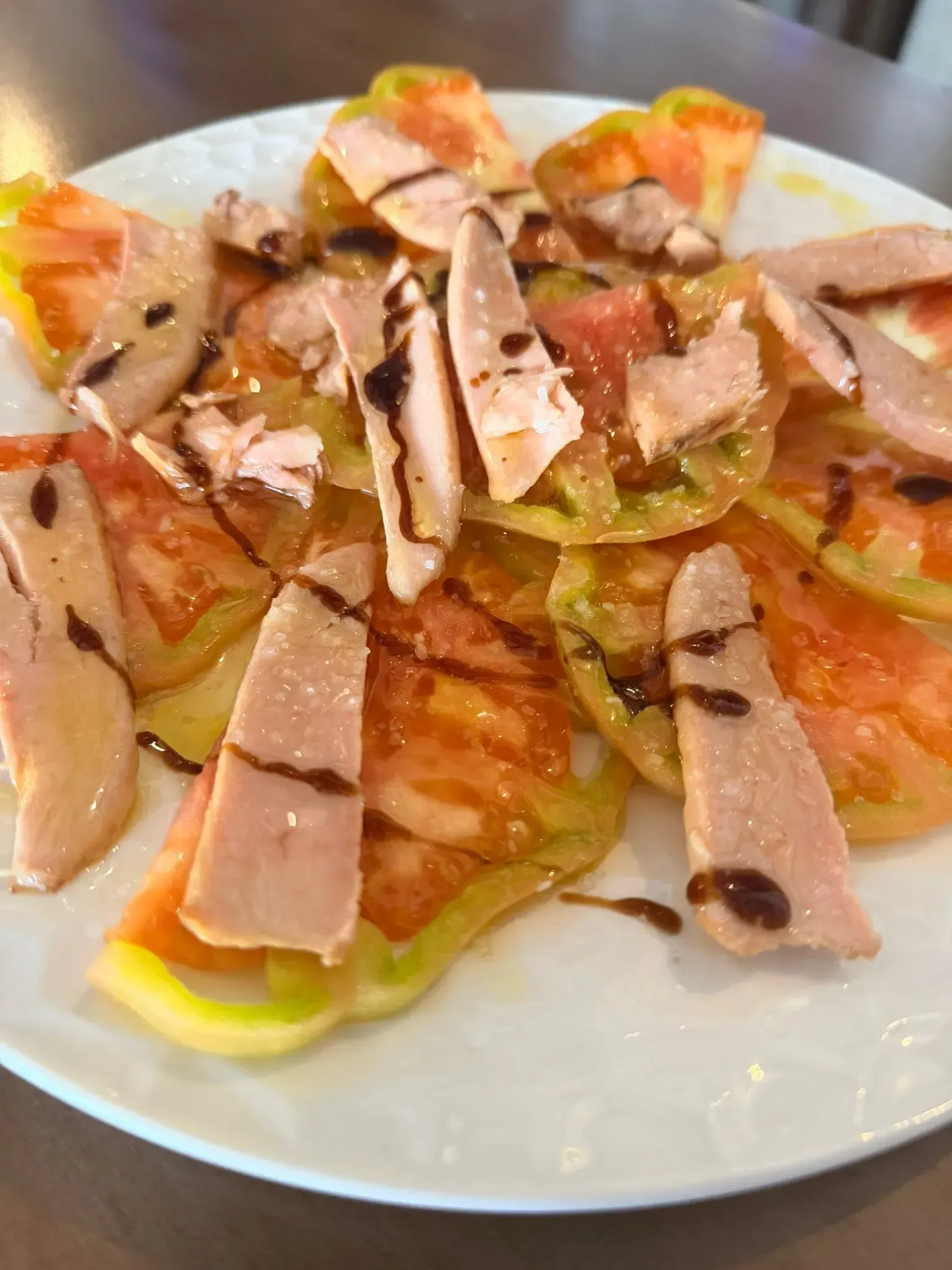 Plato de ensalada en capas cortadas en rodajas o aperitivo cubierto con jamón y salsa, en un plato blanco.