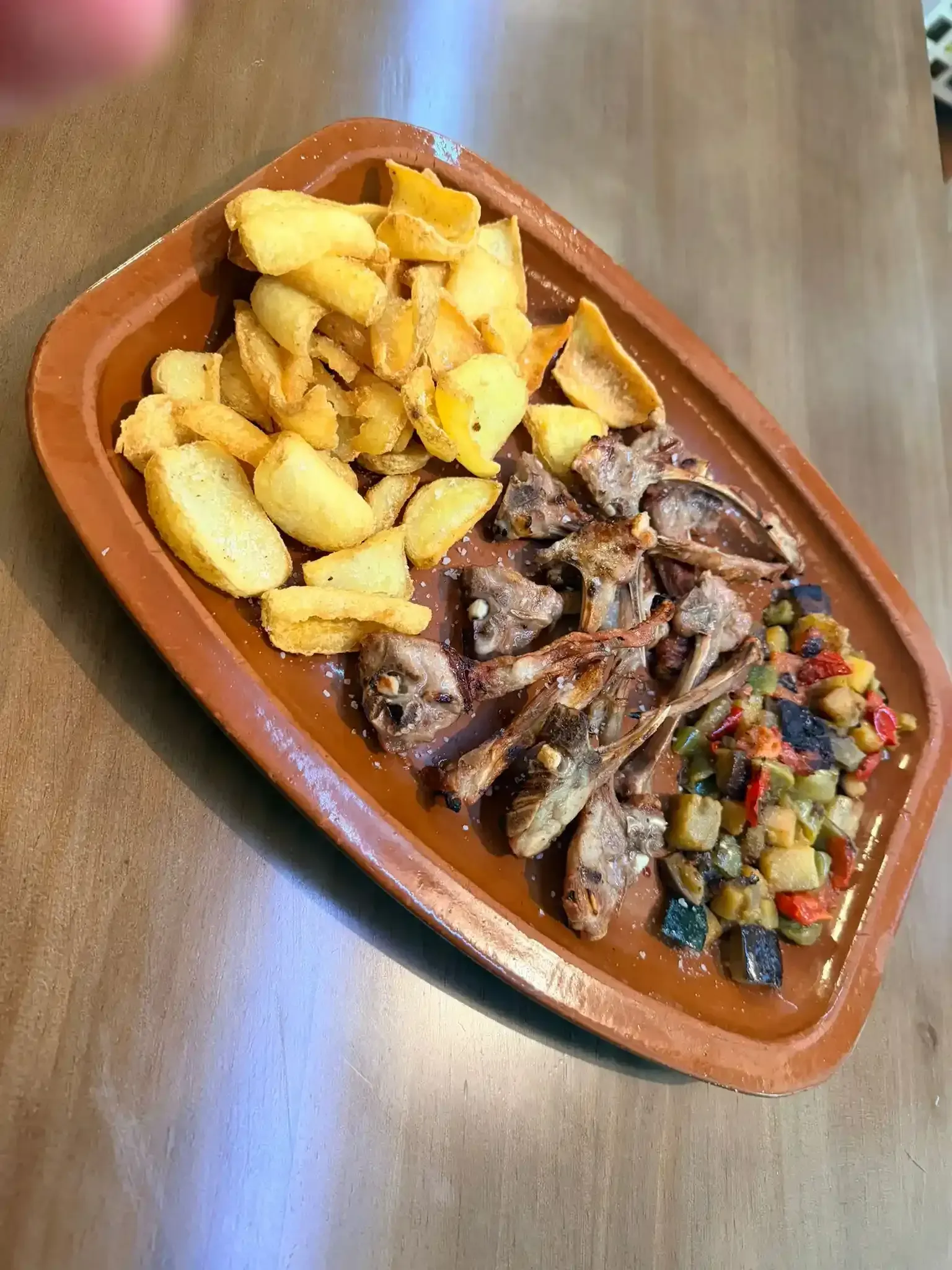 Plato de alitas de pollo asadas con patatas gajo y salsa de verduras picadas sobre una mesa de madera.