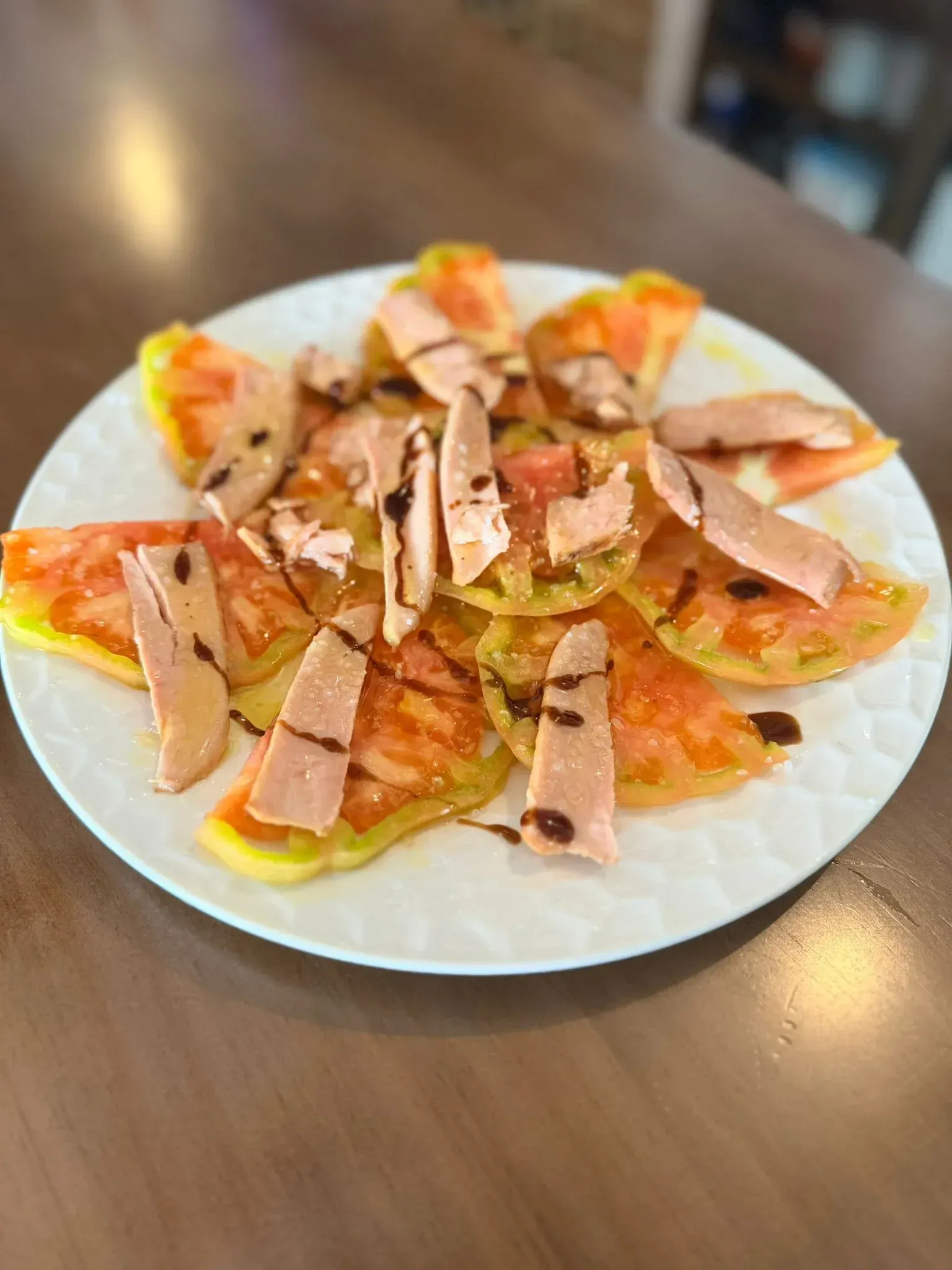 Plato blanco con fruta en rodajas y finas tiras de carne sobre una mesa de madera.