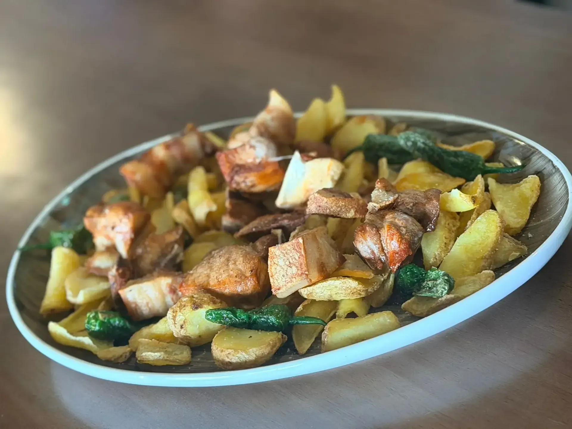 Patatas asadas y carne troceada con pimientos verdes servidas en un plato ovalado blanco.
