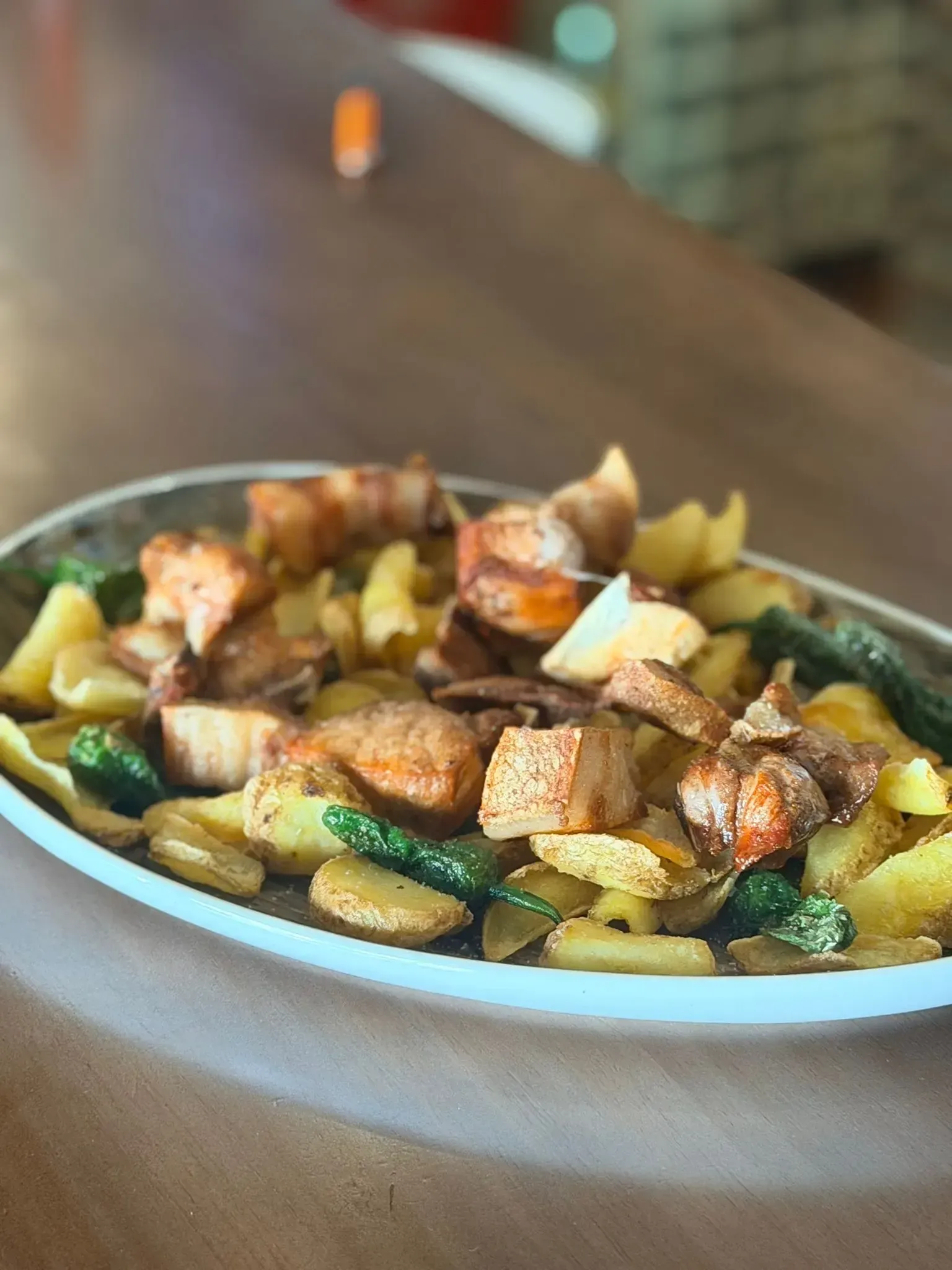 Pescado sellado a la sartén con patatas asadas y verduras verdes servido en una mesa.