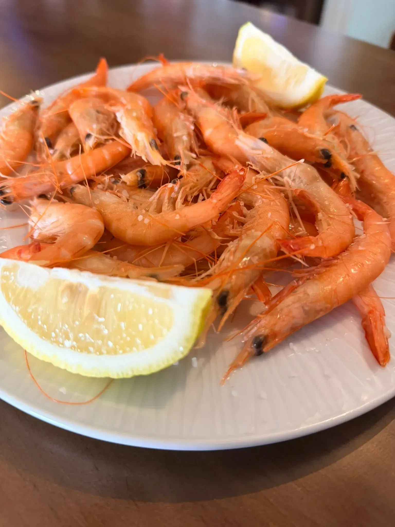 Plato de camarones cocidos adornado con rodajas de limón sobre una mesa.