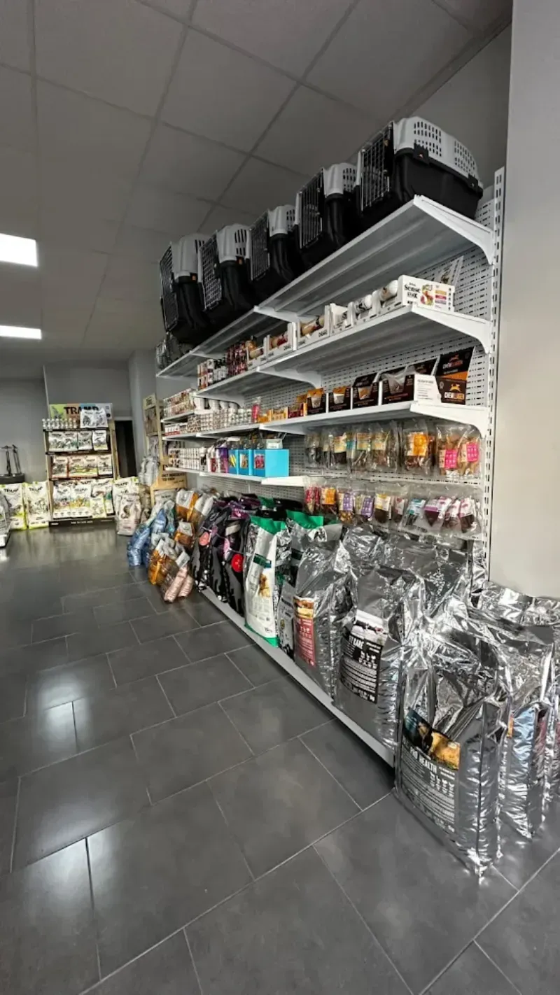Estantes repletos de alimentos y suministros para mascotas dentro de una tienda; piso y techo grises.