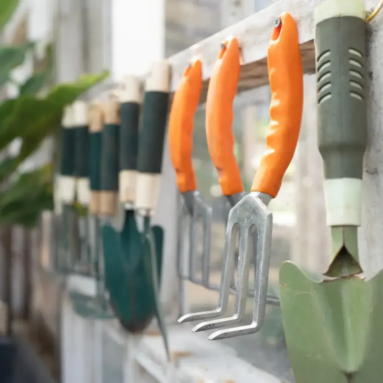 Herramientas de jardinería colgadas en un estante de madera: palas, paletas y rastrillos de mano.