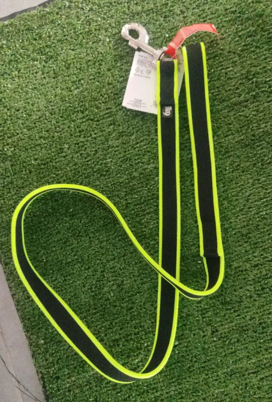 Correa para perro de color negro y amarillo neón con clip plateado sobre césped artificial.