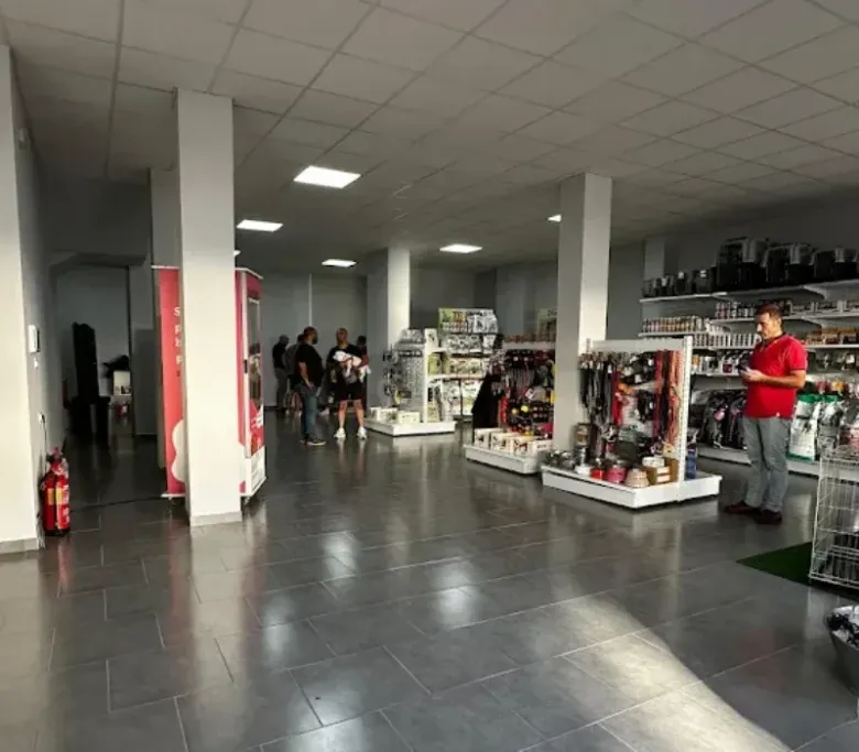 Interior de una tienda de mascotas con gente comprando. Los estantes exhiben artículos para mascotas.