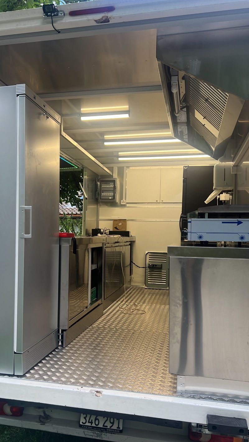 L'intérieur d'un food truck avec des appareils en acier inoxydable et un réfrigérateur.