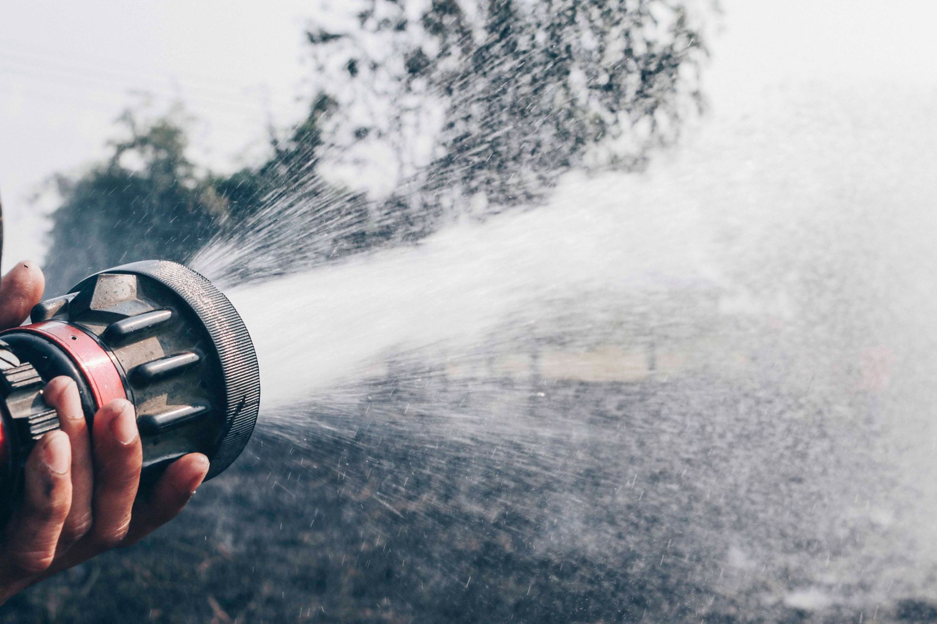 Eine Hand hält einen Feuerwehrschlauch und sprüht Wasser.