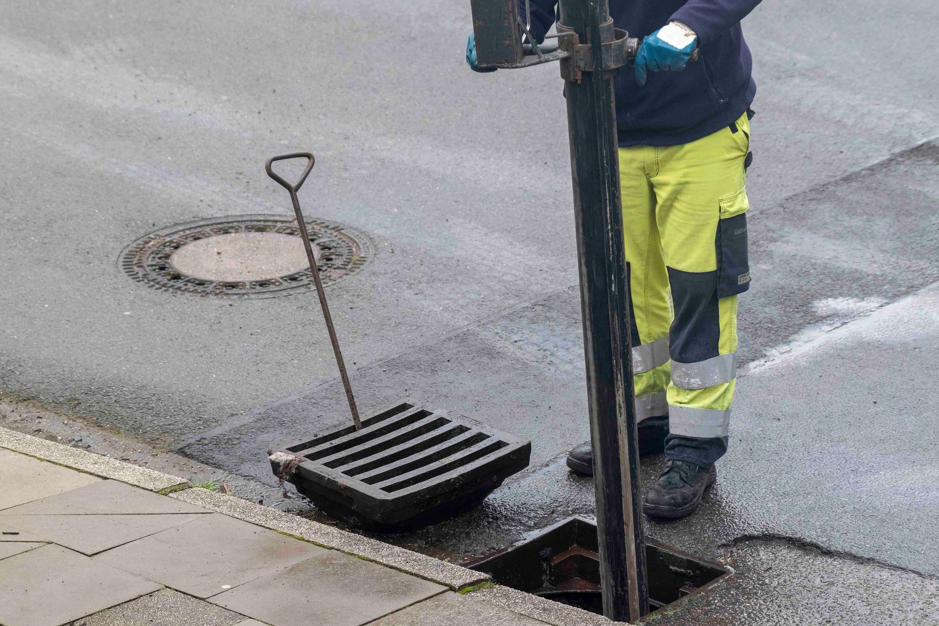 Klempner mit Handschuhen bedient einen Schraubenschlüssel an einem blauen Rohr in der Nähe eines großen Tanks in einem Hauswirtschaftsraum.