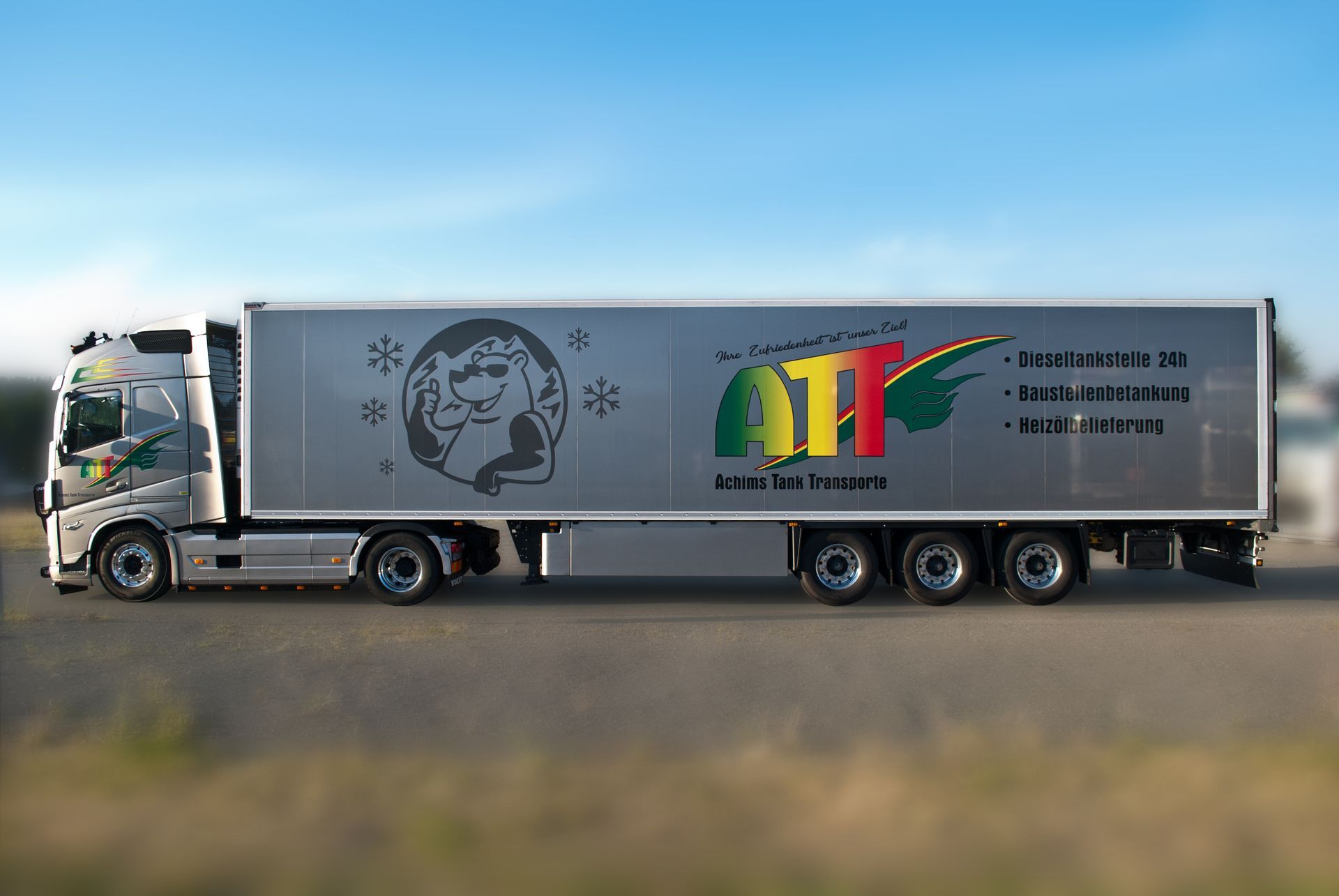 Silberner Sattelschlepper auf einer Straße mit „ATI“-Logo und Text auf dem Anhänger.
