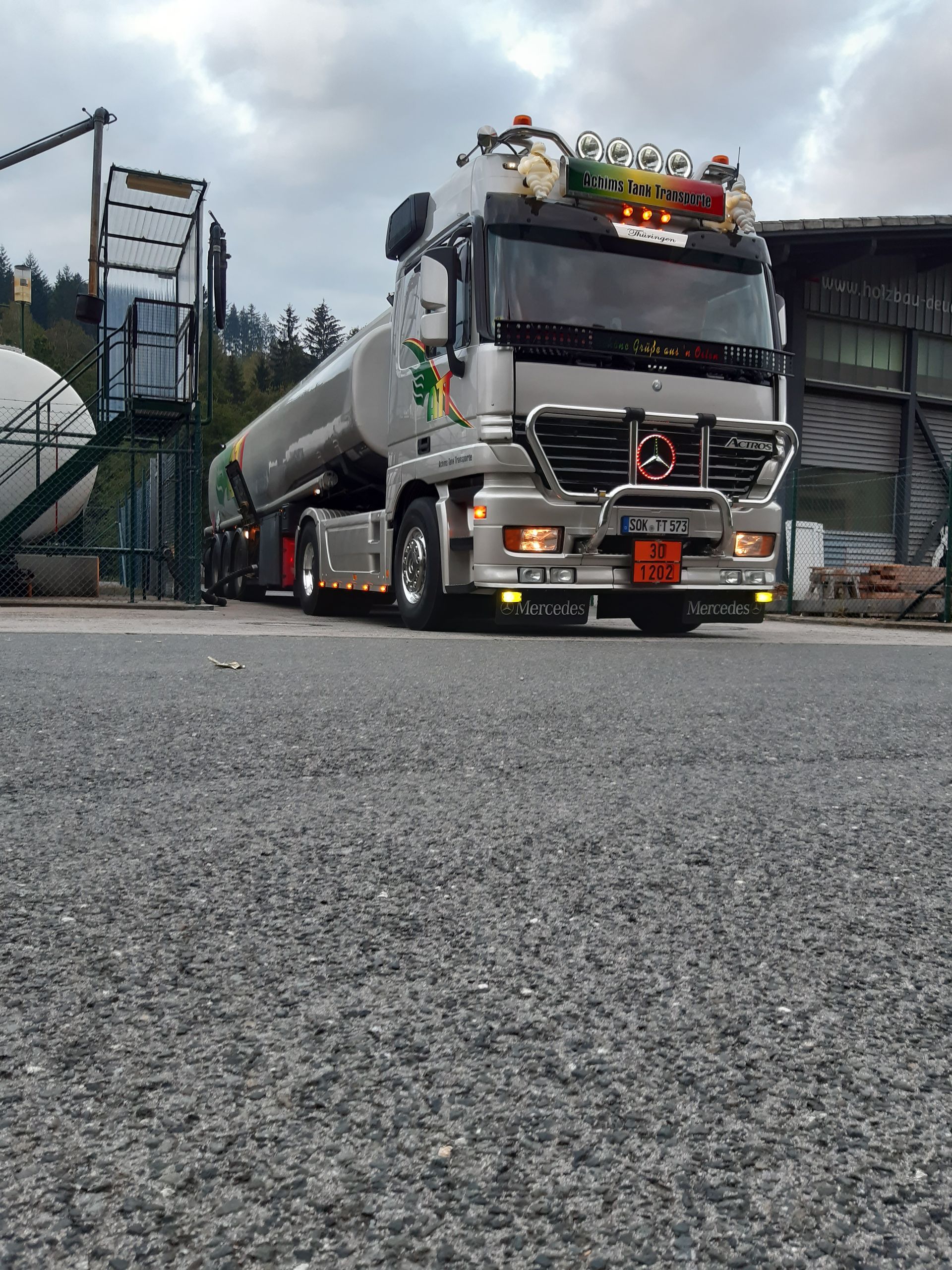 Silberner Tanklastwagen, der unter einem bewölkten Himmel auf Schotter geparkt ist.