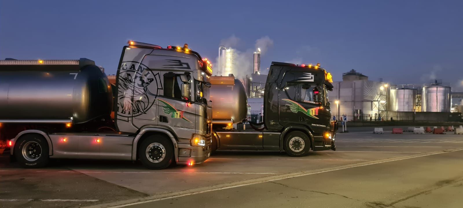 Zwei nachts geparkte Tanklastwagen, im Hintergrund Industrieanlagen.