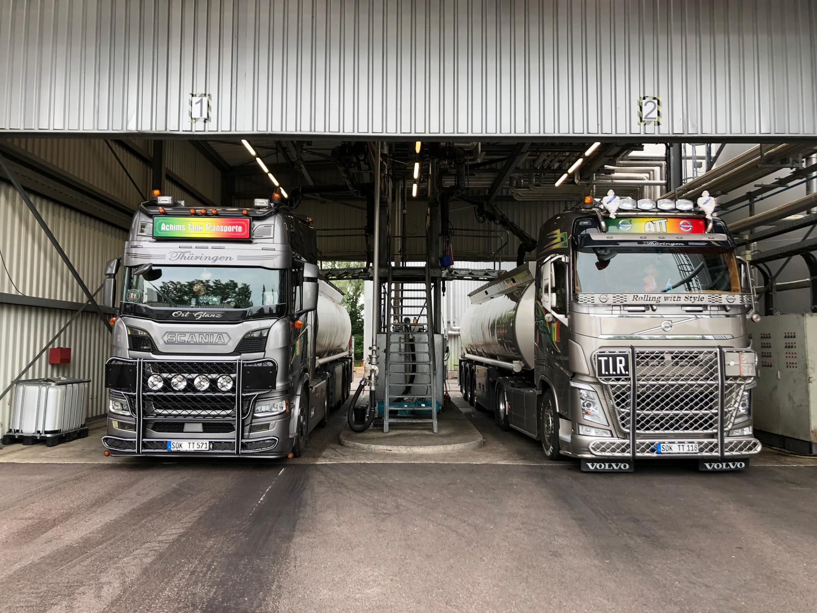 Zwei silberne Tanklastwagen parkten unter einer Laderampe.